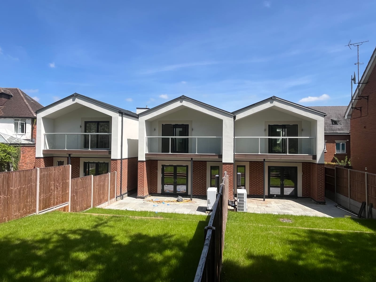 Three Harpenden homes seen from the gardens, white render over brick with glass balconies